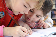 Two children looking intensely at a paper while one child is writing on it.