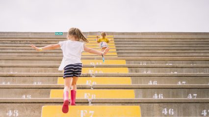 Two caucasian blondes kids running up a bleachers stairs with water boots