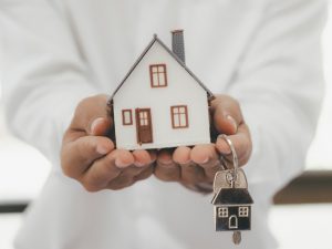 Person holding a tiny figure of a home and holding with a key-ring that is shaped like a house