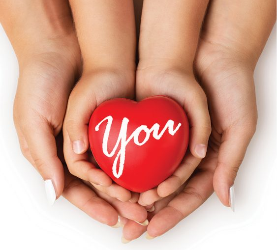 Image of a mothers hands with child's hands on top. The child is holding a heart-shaped figure with the word You written on it.