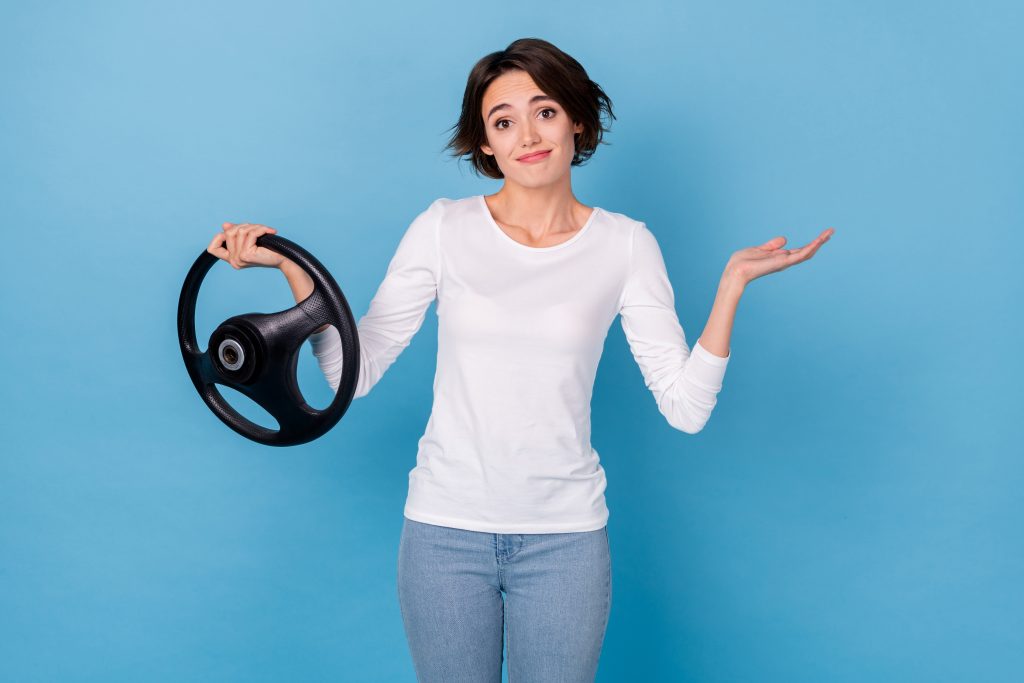 Photo of pretty positive lady failing driving exam hold steering wheel shrug shoulder isolated on blue color background.