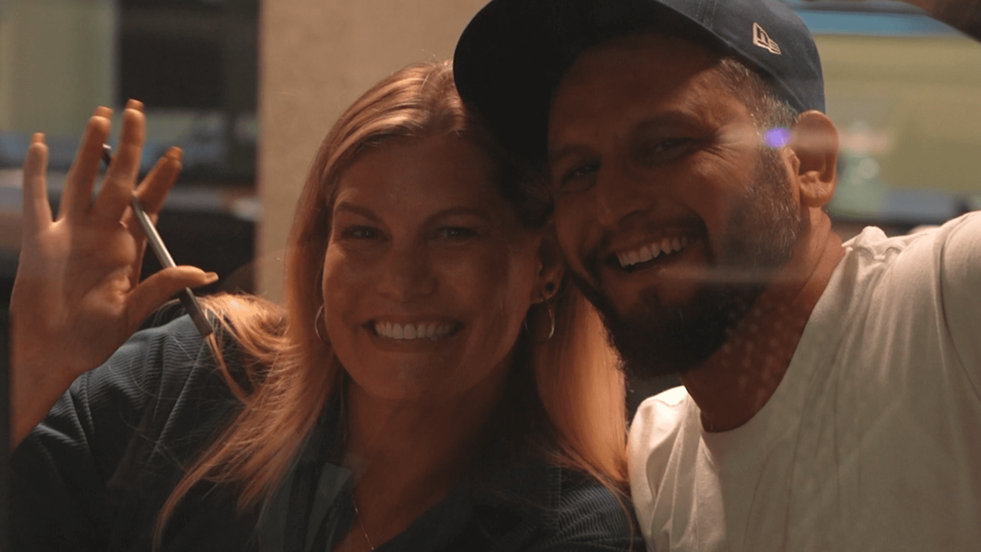 Two people waving and smiling through a glass window.